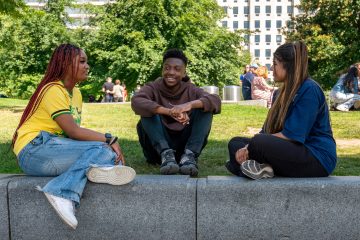 Three young people sat in a park smiling together, ready to go into youth leadership