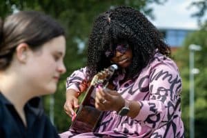 Young woman with curly hair playing guitar during mental health outreach event.