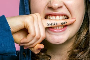A young person biting their finger with writing on it saying 'shut up'