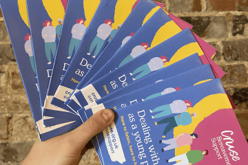 A hand holding a fan of flyers - the first-ever youth-led bereavement guide. The tip of the iceberg of how Cruse are shaping services with young people