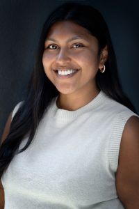 Portrait of Priya Shah, a professional woman with a warm smile, representing participation and diver.