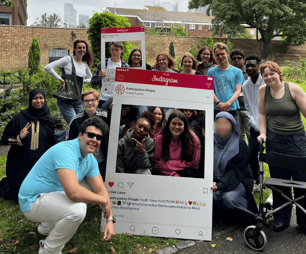 Diverse youth group outdoors holding social media frame for Participation People.