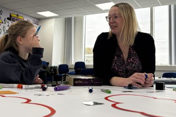 A senior leader and young girl sat at a table talking and co-producing resources, improving safeguarding thresholds.