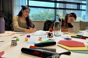 two people working at a table covered in pens and coloured paper as part of their youth engagement training